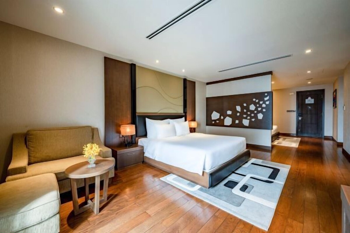 Een moderne hotelkamer met een groot bed, een bank, een klein tafeltje met een vaas en een decoratief wandobject.