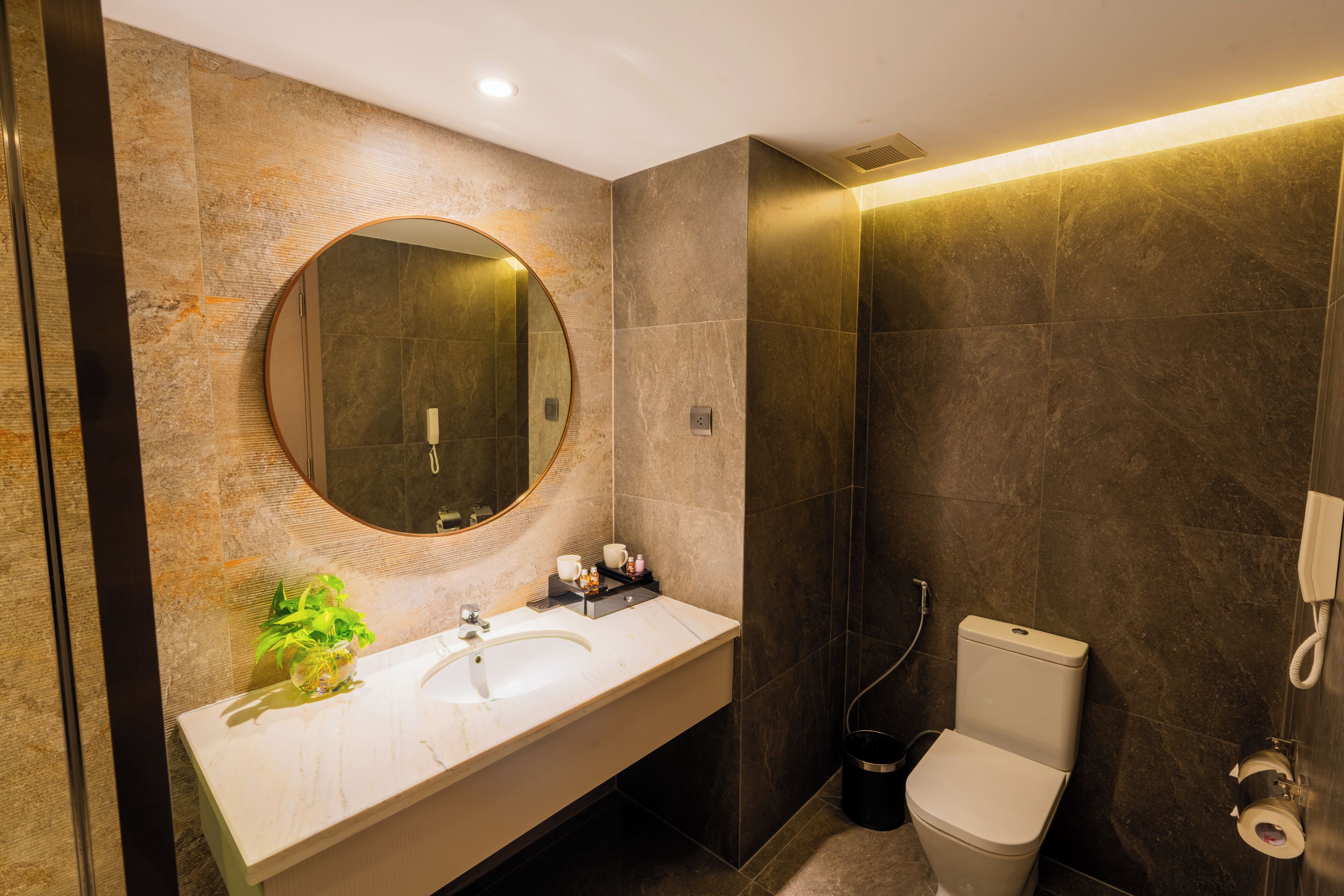 Une salle de bain moderne avec un grand miroir rond, un lavabo blanc, des toilettes et un espace douche.