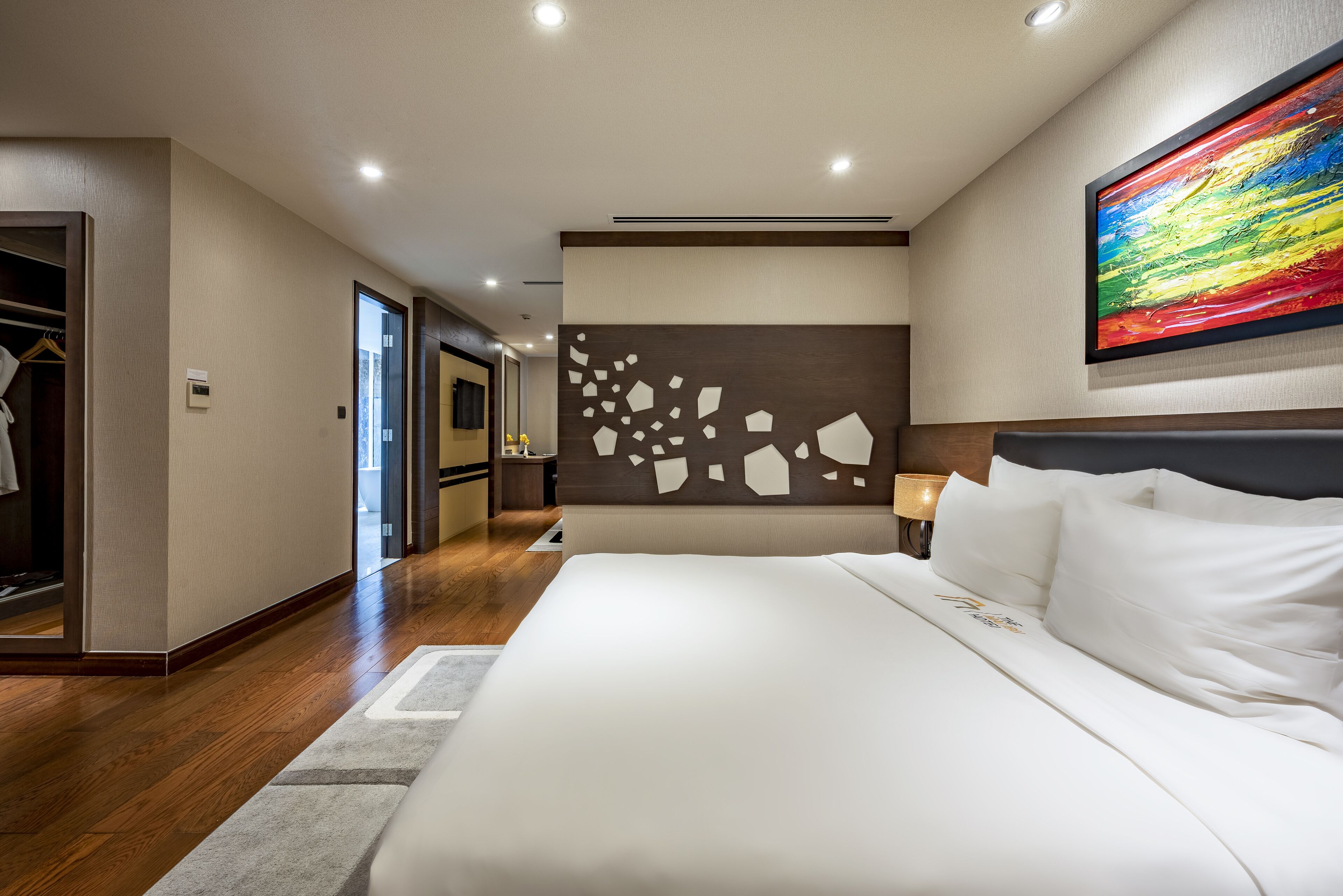 Una habitación de hotel moderna con una cama grande, un vestidor amplio y un elemento decorativo en la pared.
