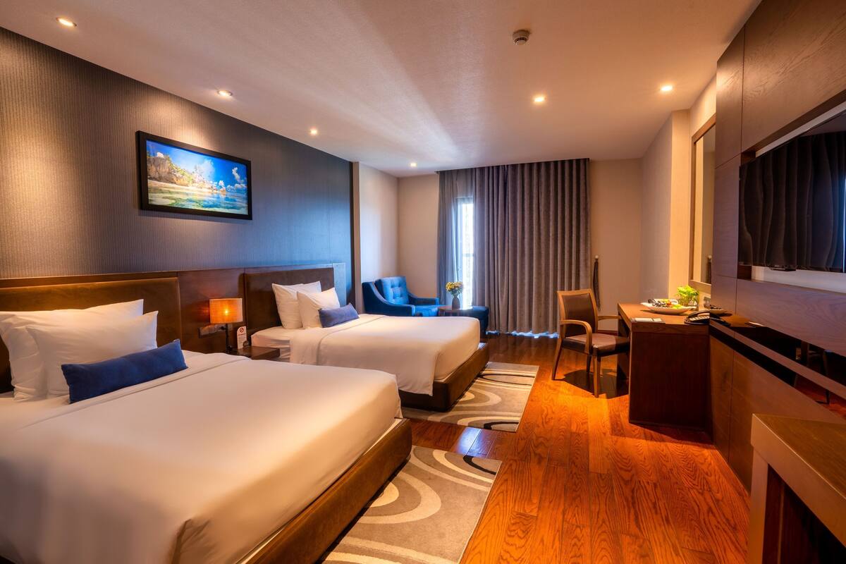 Ein Hotelzimmer mit zwei Betten, einem Schreibtisch, einem Sessel, einem Fernseher und einem Bild an der Wand.