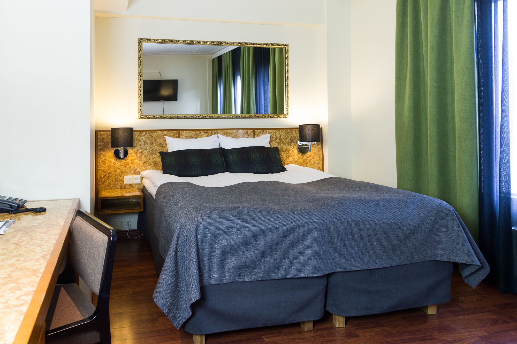 A hotel room with a bed, a desk, a telephone, and a mirror.