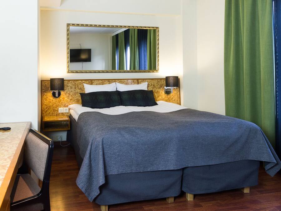 A hotel room with a bed, a desk, a telephone, and a mirror.