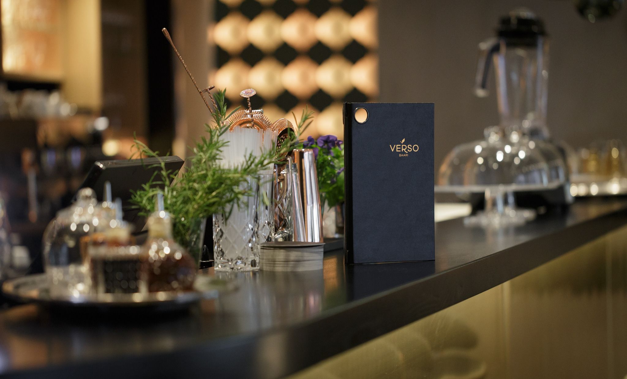 A bar area with a black card labeled 'Verso Baari' and various bar tools and glassware.
