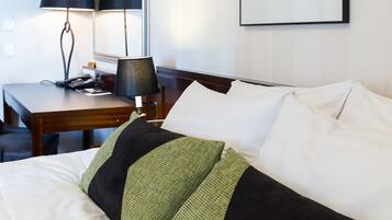 A hotel room with a neatly made bed, a desk with a lamp, and a map on the wall.