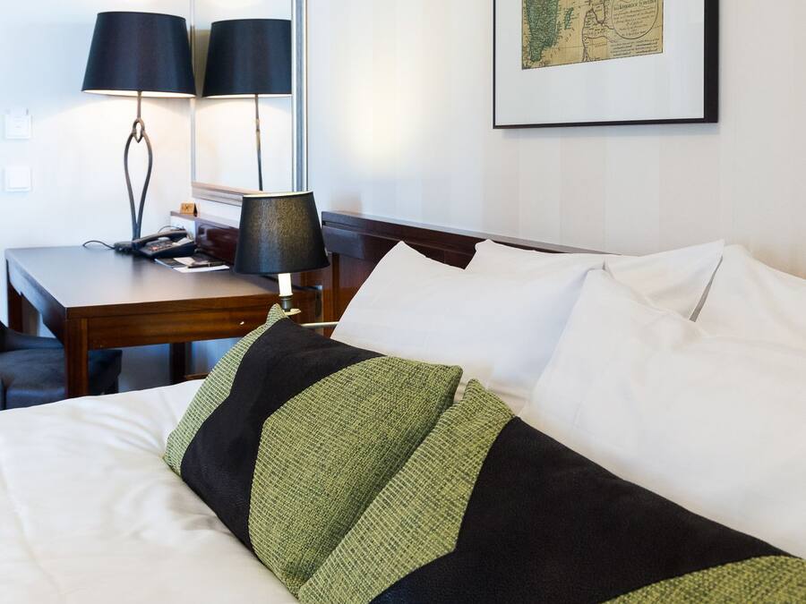 A hotel room with a neatly made bed, a desk with a lamp, and a map on the wall.