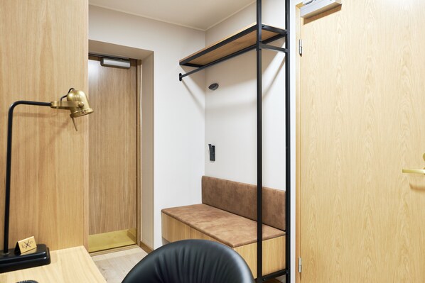 Habitación pequeña con un banco de madera, un escritorio con lámpara y una puerta con marco de metal negro.