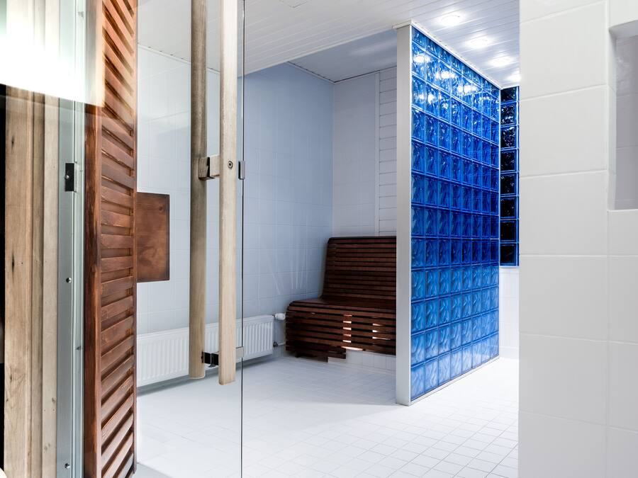 Une salle de bain moderne avec un banc en bois, des murs recouverts de carreaux blancs et une cloison en verre bleu.