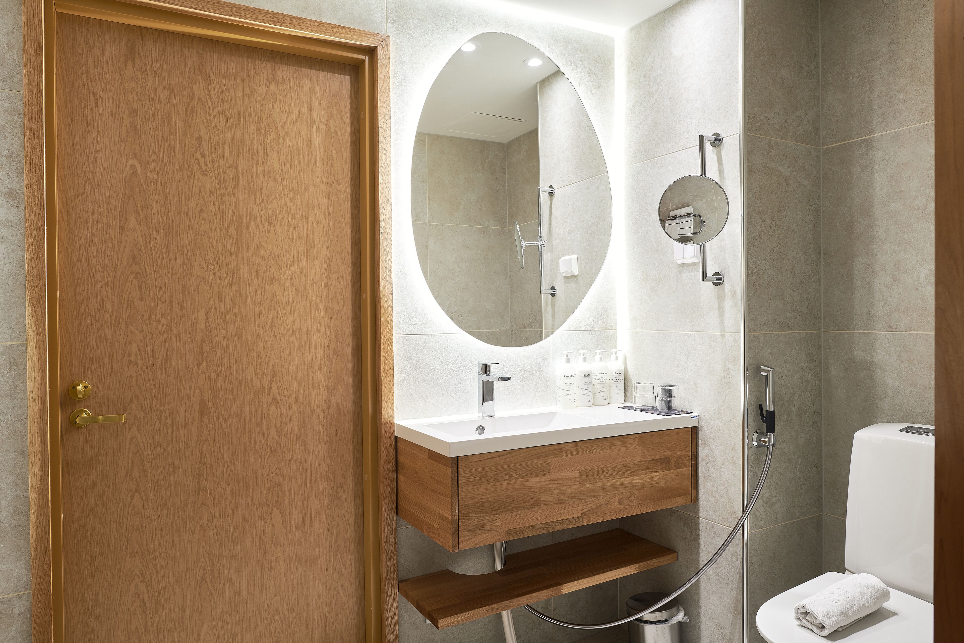 A modern bathroom with a wooden door, a white sink with a mirror, and a shower area.