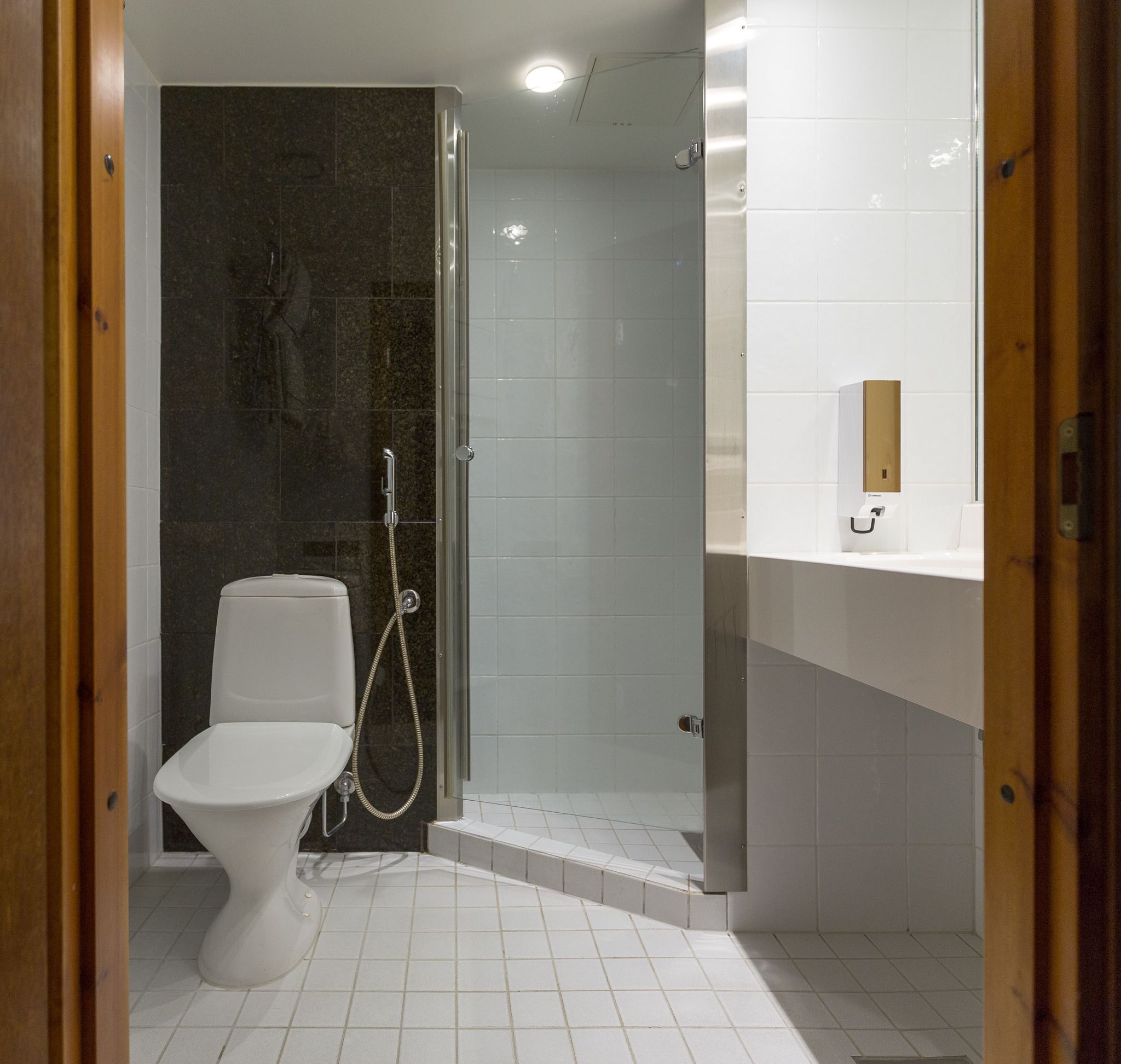 A modern bathroom with a toilet, shower, and a white tiled floor.