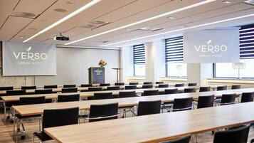 A conference room with multiple tables and chairs, large banners with the hotel name, and a podium with a flower arrangement.
