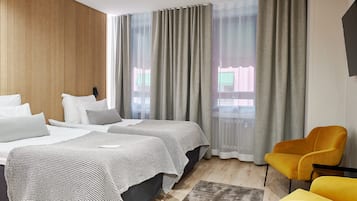 A hotel room with two beds, a yellow armchair, and large windows with sheer curtains.