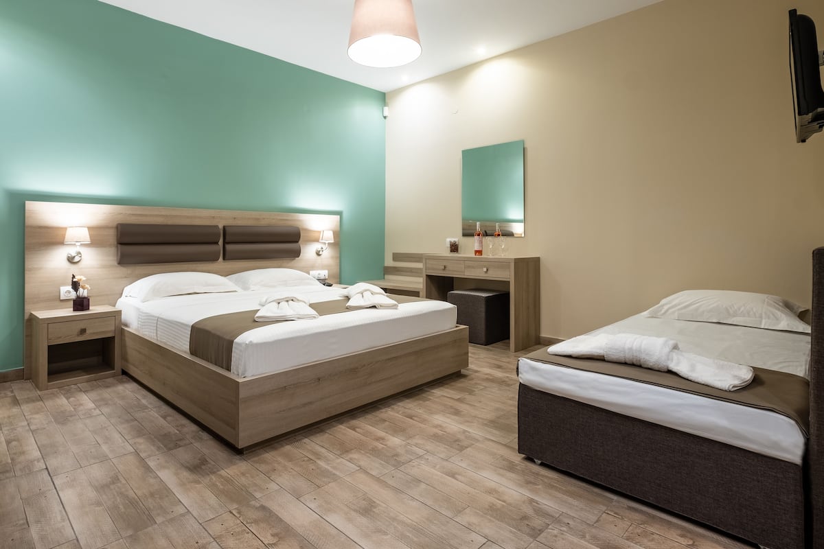 A modern hotel room with a large bed, a smaller bed, a desk, and a mirror.