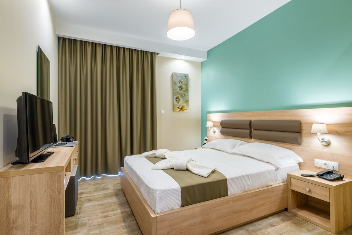 A hotel room with a bed, bedside table, lamp, and a TV on a desk.