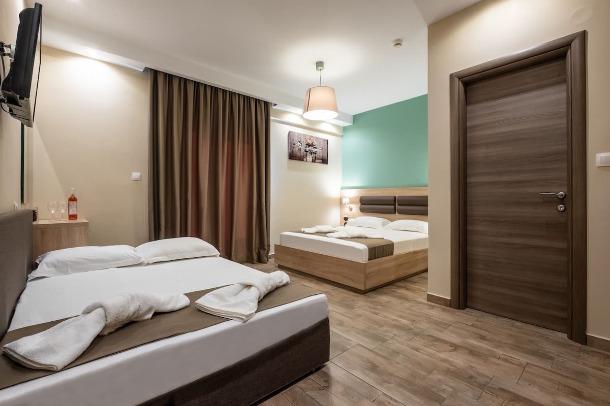 A hotel room with a large bed, a smaller bed, a TV, a door, and a painting on the wall.