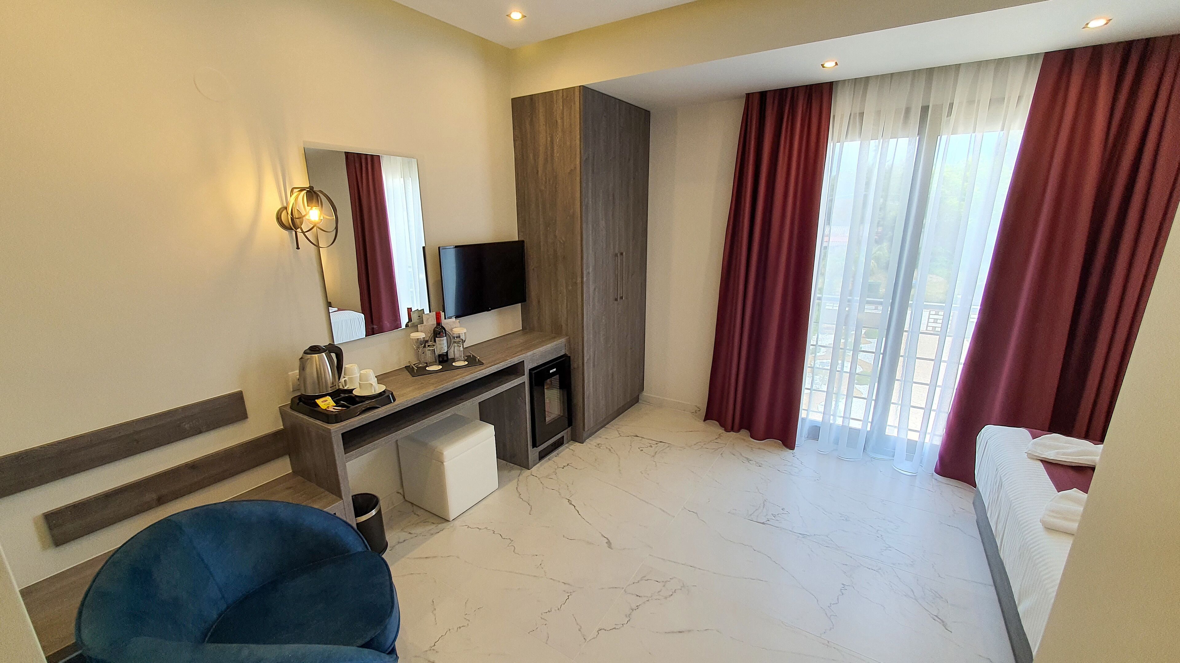 Une chambre d’hôtel comprenant un lit, un bureau avec un téléviseur à écran plat, une machine à café et une grande fenêtre avec des rideaux.