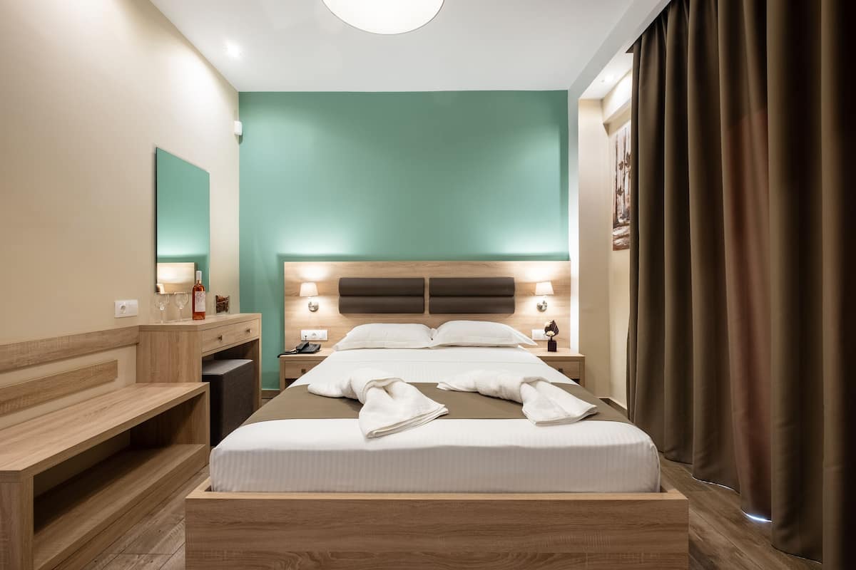 A modern hotel room with a large bed, wooden headboard, bedside tables, and a mirror.