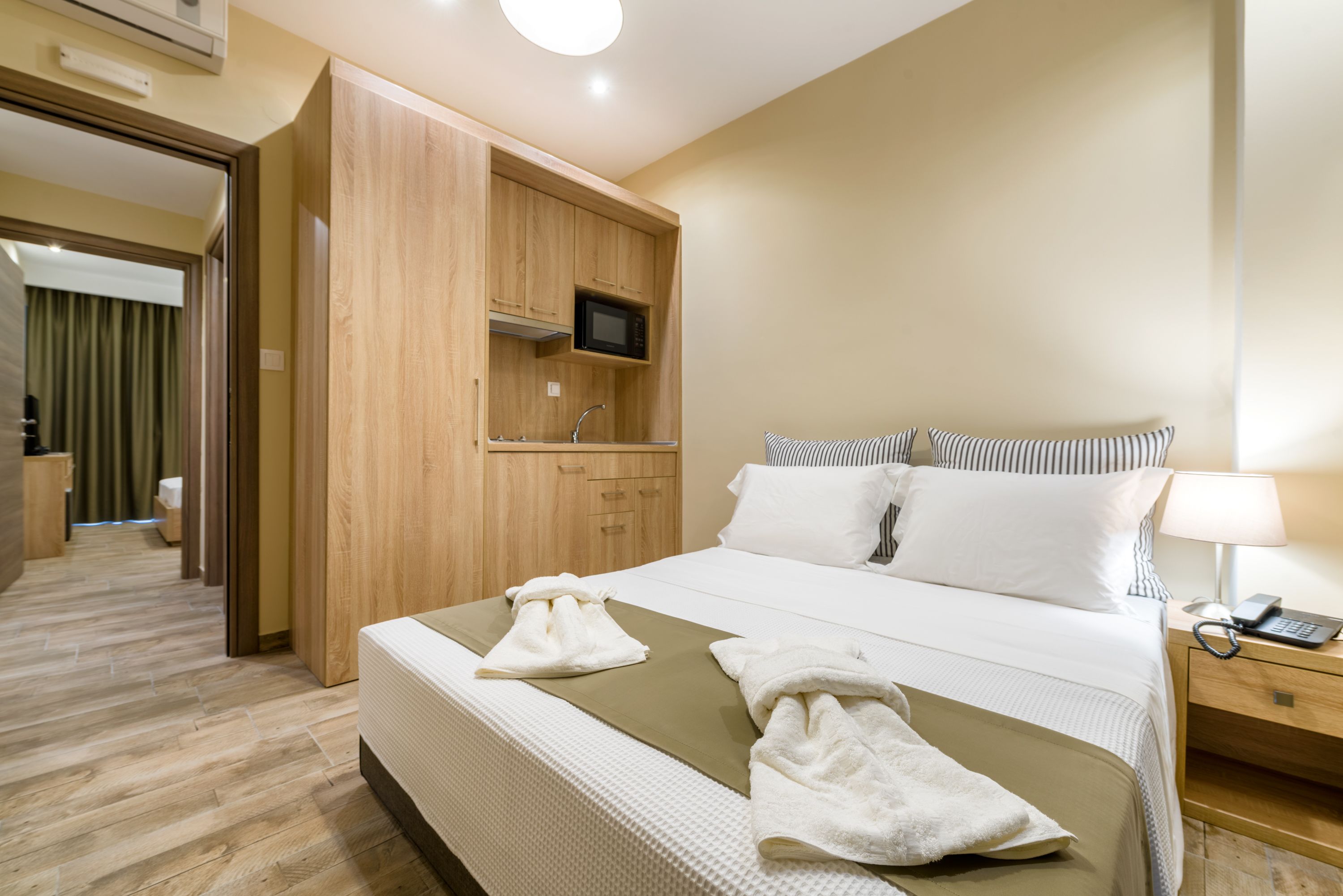 A hotel room with a bed, a wooden wardrobe, a television, and a bedside table with a lamp and phone.