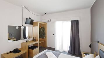 Ein modernes Hotelzimmer mit Bett, Schreibtisch aus Holz, Kleiderschrank, Fernseher und einem Fenster mit Vorhängen.