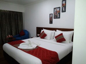 A hotel room with a large bed, a blue chair, and three framed pictures on the wall. - The Royal Comfort (Bengaluru)