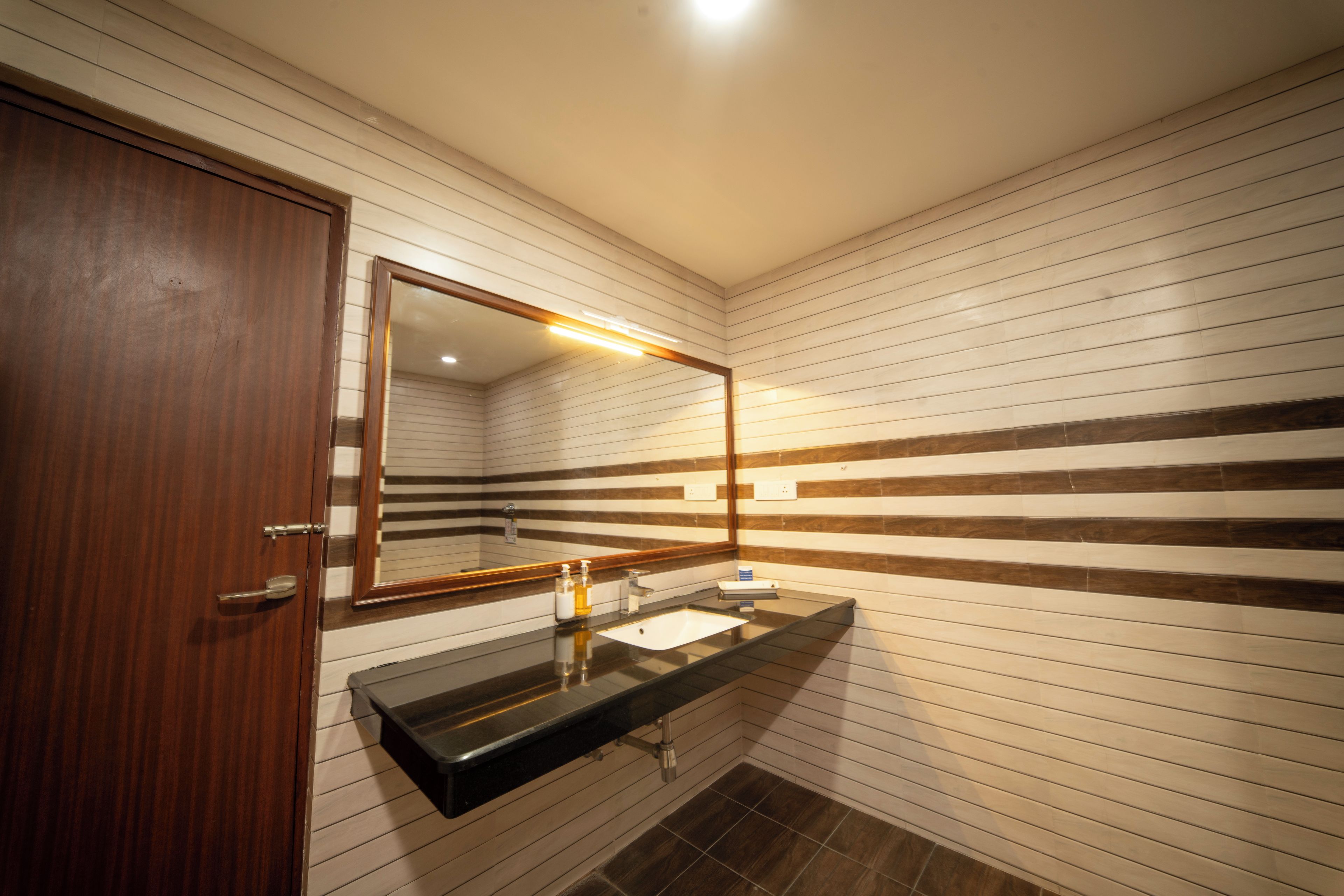 Un baño con puerta de madera, un espejo, un lavabo y azulejos rayados en la pared.