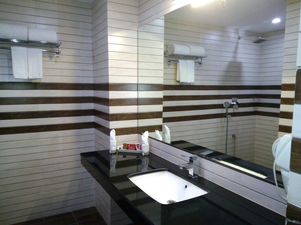Un baño moderno con paredes de azulejos a rayas, un lavabo negro y un espejo grande.