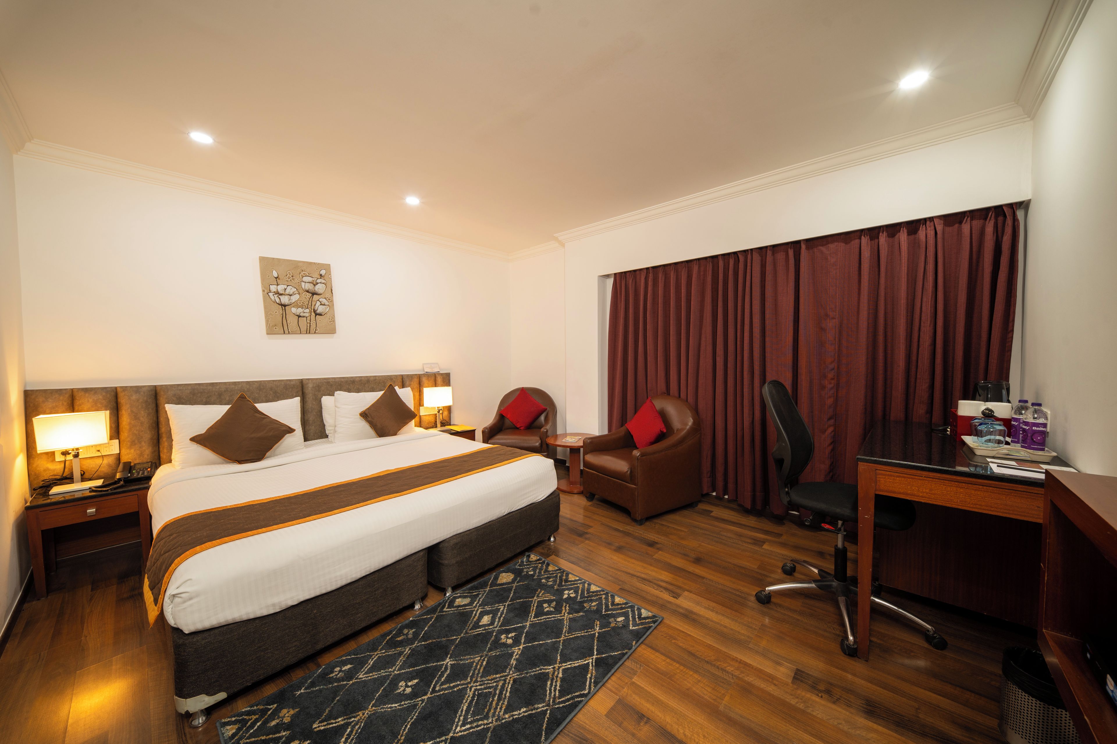 Habitación de hotel con una cama grande, un escritorio, una silla, una mesita y un ventanal con cortinas.