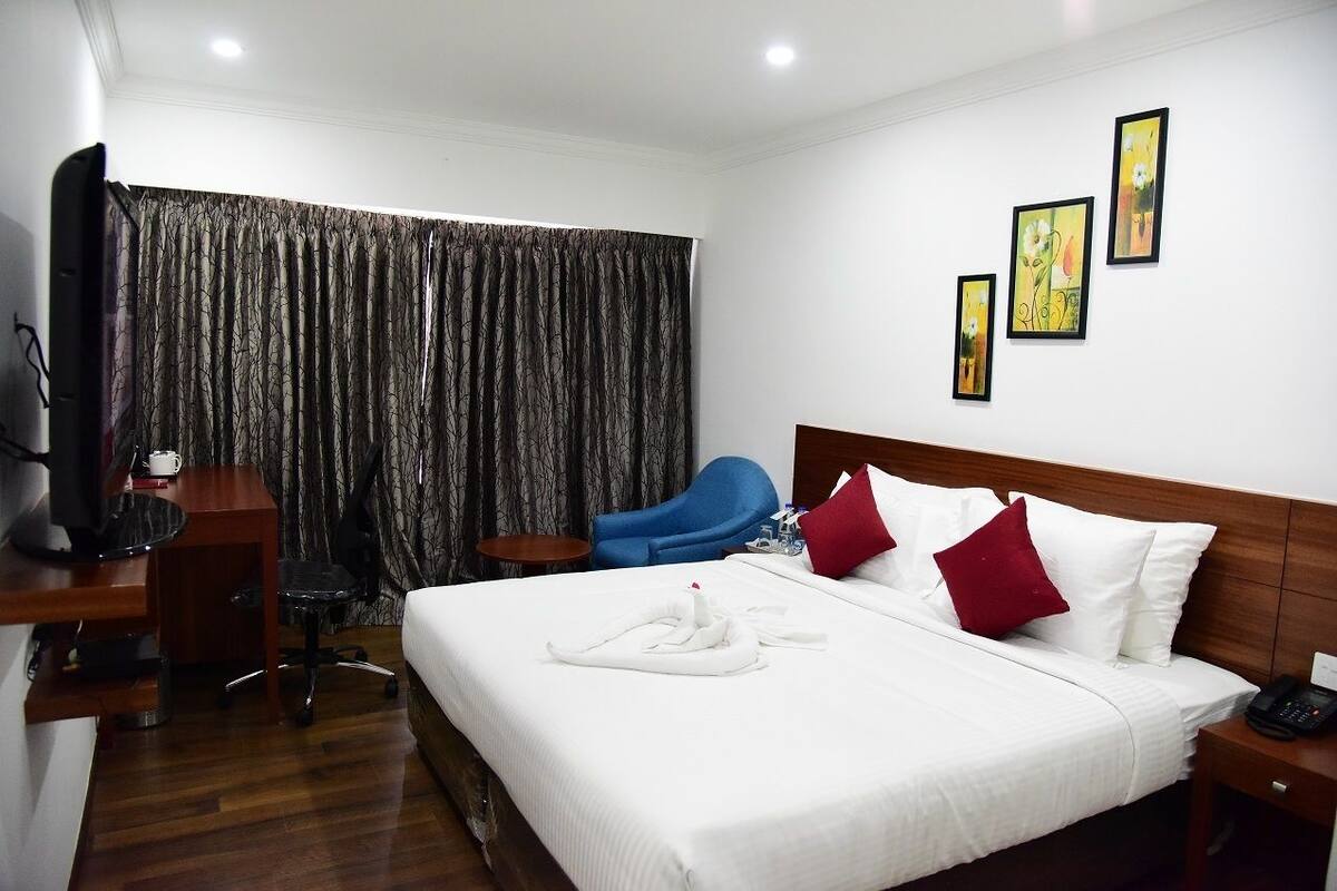 A hotel room with a neatly made bed, a desk with a computer, a chair, and a TV.