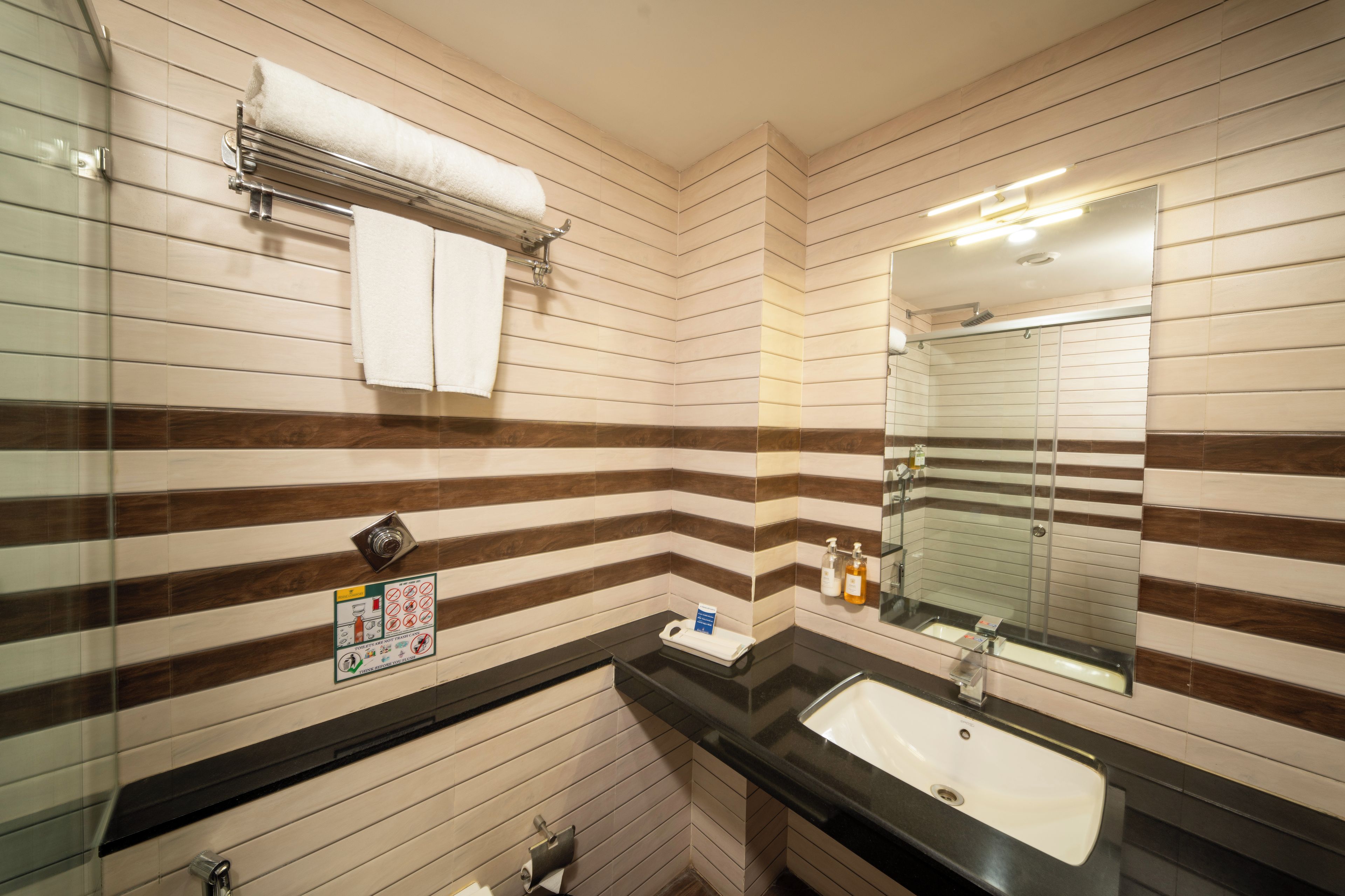 A bathroom with striped tile walls, a sink, a mirror, and a towel rack.