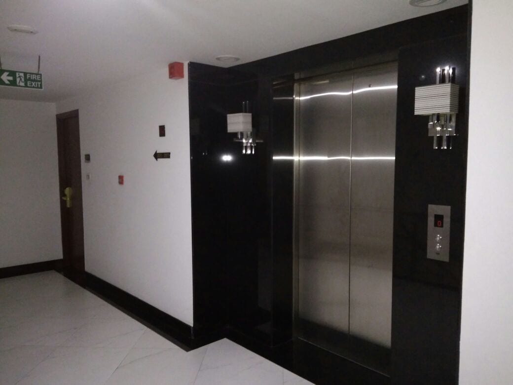An elevator with a digital display, a fire exit sign, and directional arrows on the wall.