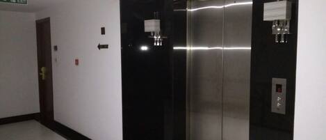 An elevator with a digital display, a fire exit sign, and directional arrows on the wall.