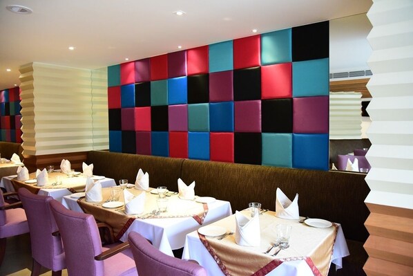 A restaurant with tables set for dining, a colorful wall design, and a modern interior.