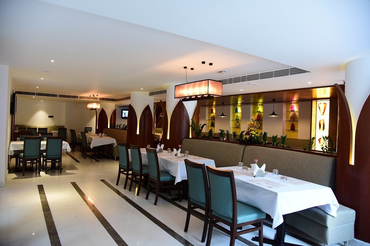 Un restaurante con mesas dispuestas para comer, una barra alargada y una pared decorativa con luces.