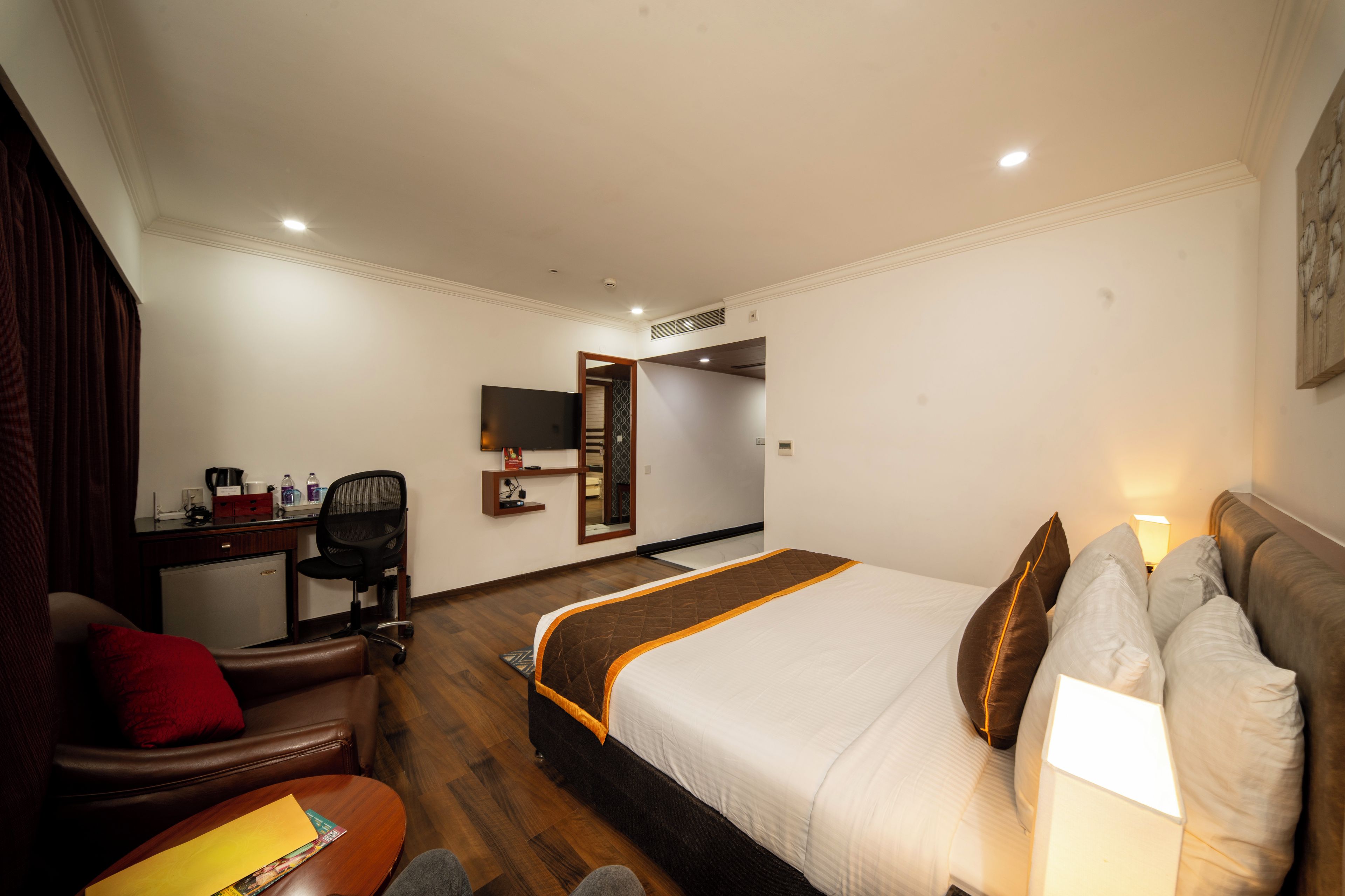 Habitación de hotel con cama, escritorio, silla, televisor y espejo.