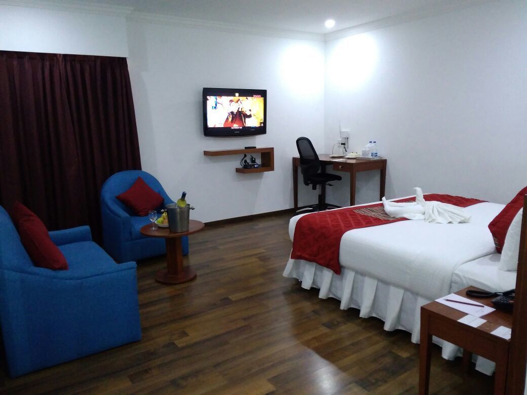 Ein Hotelzimmer mit einem Bett, einem blauen Sessel, einem Schreibtisch, einem Fernseher und Holzboden.