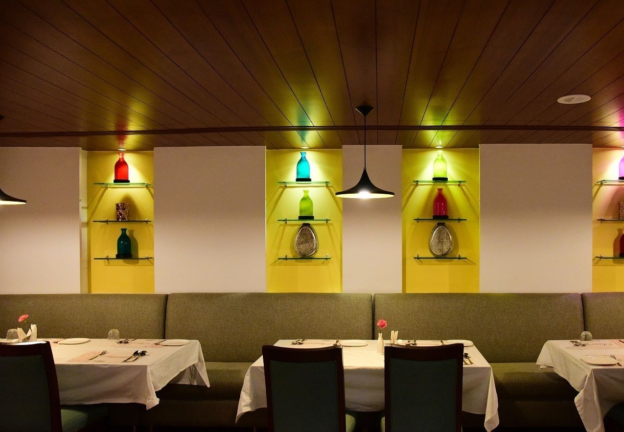 A restaurant with booths and tables, each with a white tablecloth and set with cutlery.