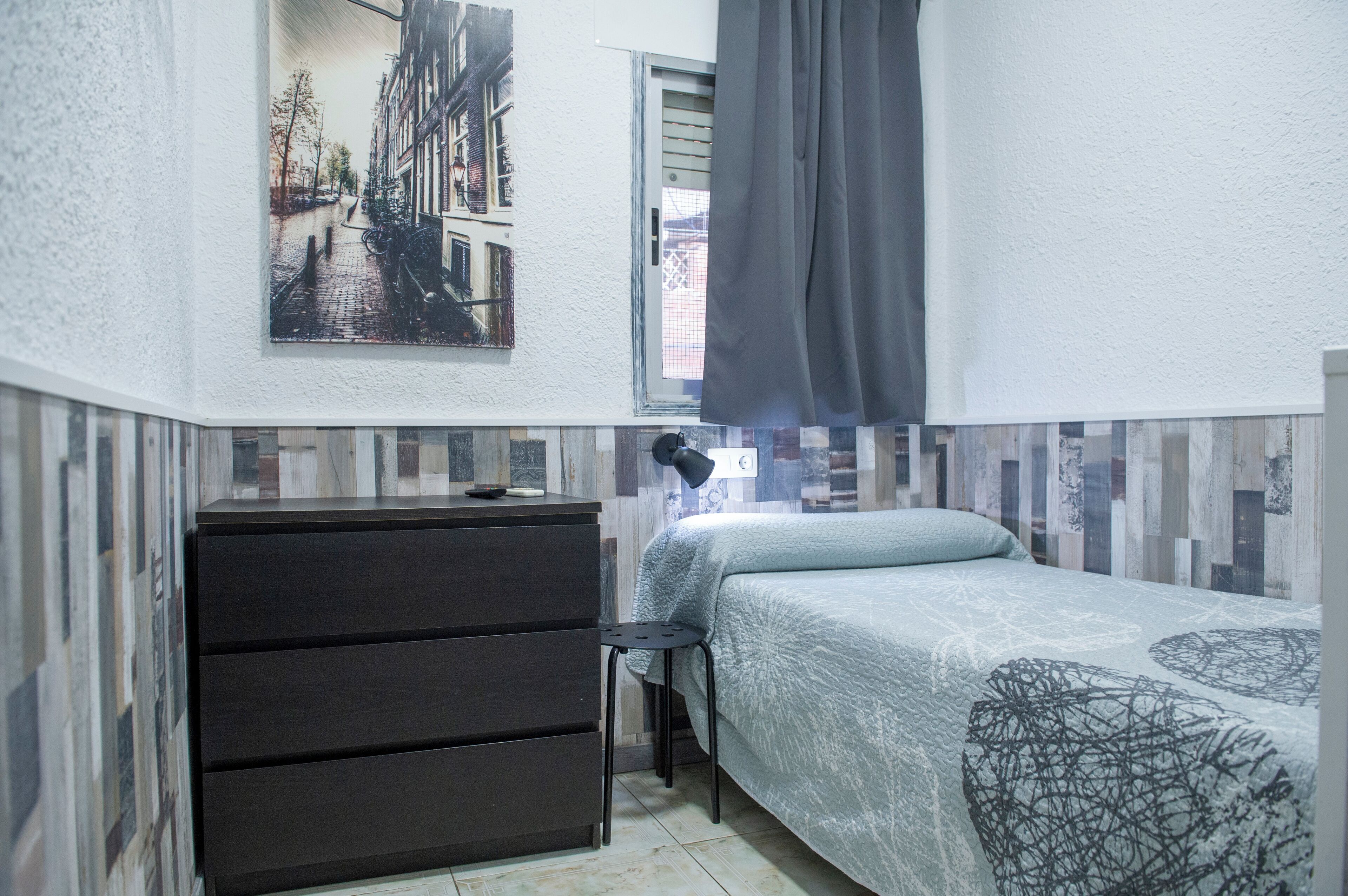 Un dormitorio pequeño y ordenado con una cama, un tocador y una ventana con cortinas.
