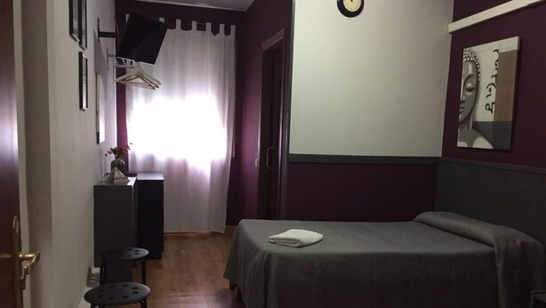 Une chambre d’hôtel avec un lit, un bureau, une chaise, une télévision et une horloge au mur.