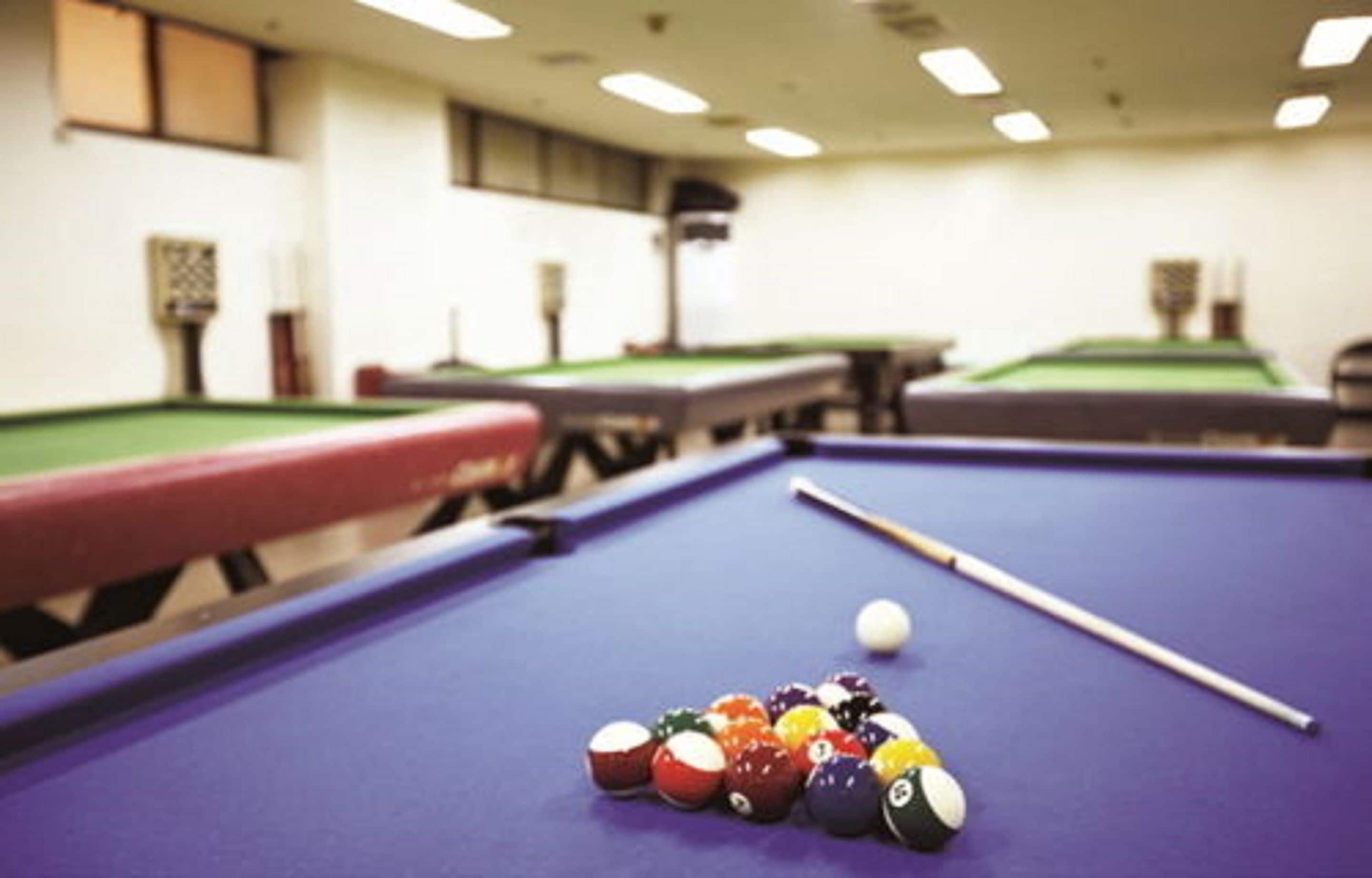 A pool table with balls and a cue stick in a room with other pool tables.