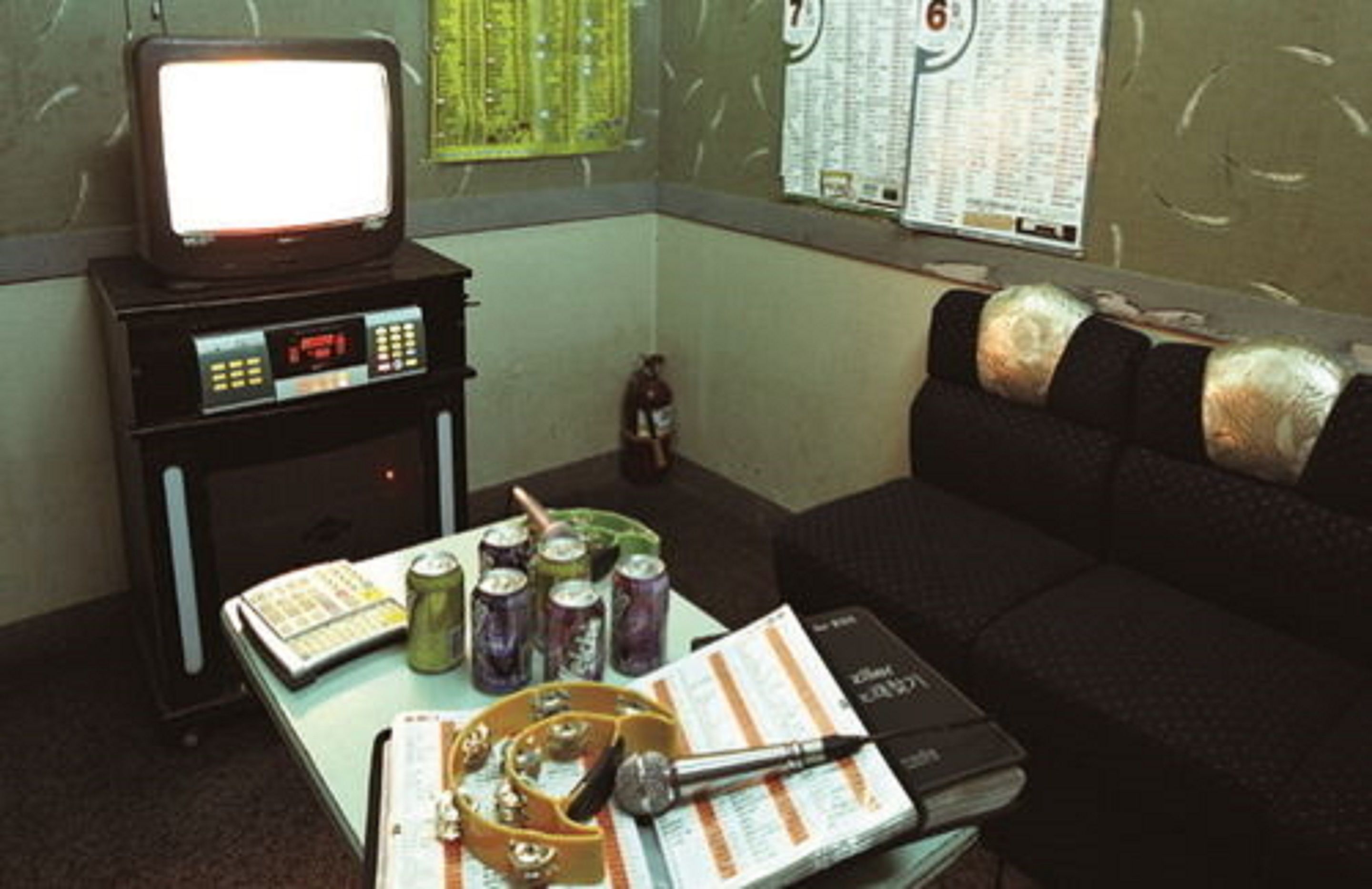 Una stanza con una televisione su un mobile, un tavolo con lattine, un libro e una penna.