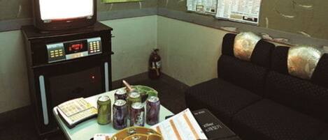 Una habitación con una televisión sobre un mueble bajo, una mesa con latas, un libro y un bolígrafo.