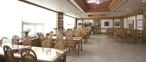 A spacious dining area with multiple tables and chairs, a high ceiling with a fan, and large windows allowing natural light.