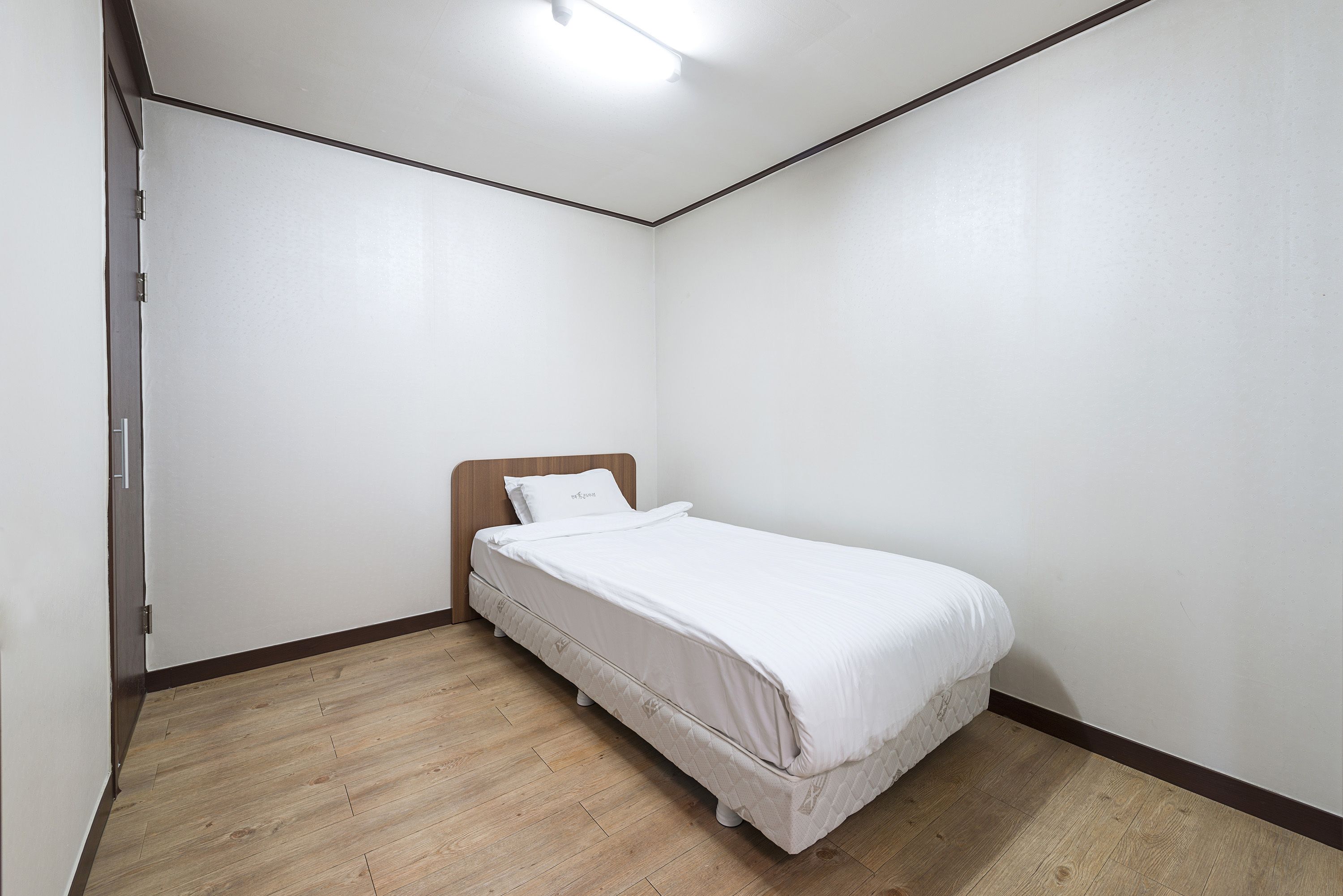 A small, neatly arranged bedroom with a single bed, wooden flooring, and white walls.