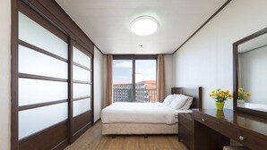 Een hotelkamer met een bed, een bureau, een spiegel en een raam met uitzicht op gebouwen.
