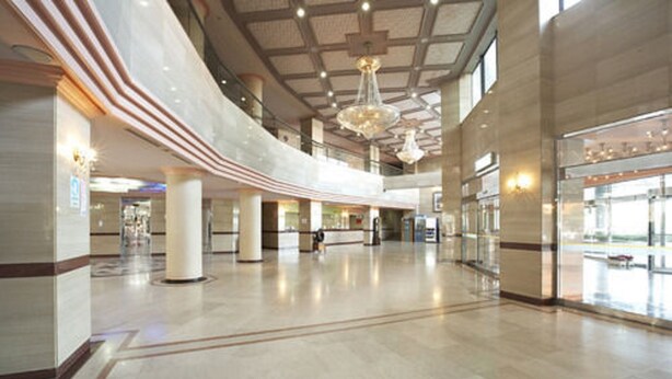 Een ruime lobby met hoge plafonds, grote zuilen en moderne kroonluchters.