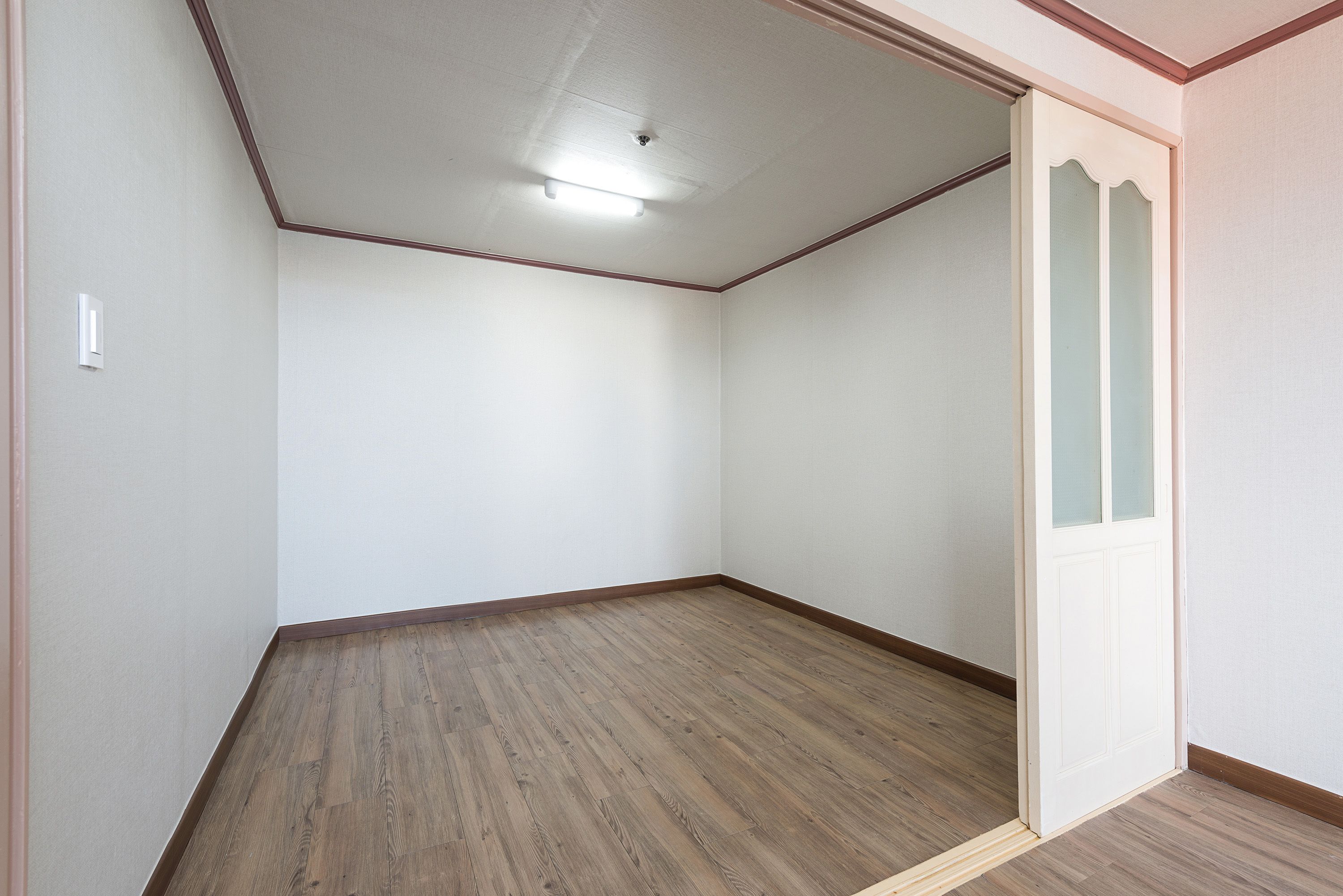 A room with wooden flooring, white walls, and a door with frosted glass panels.