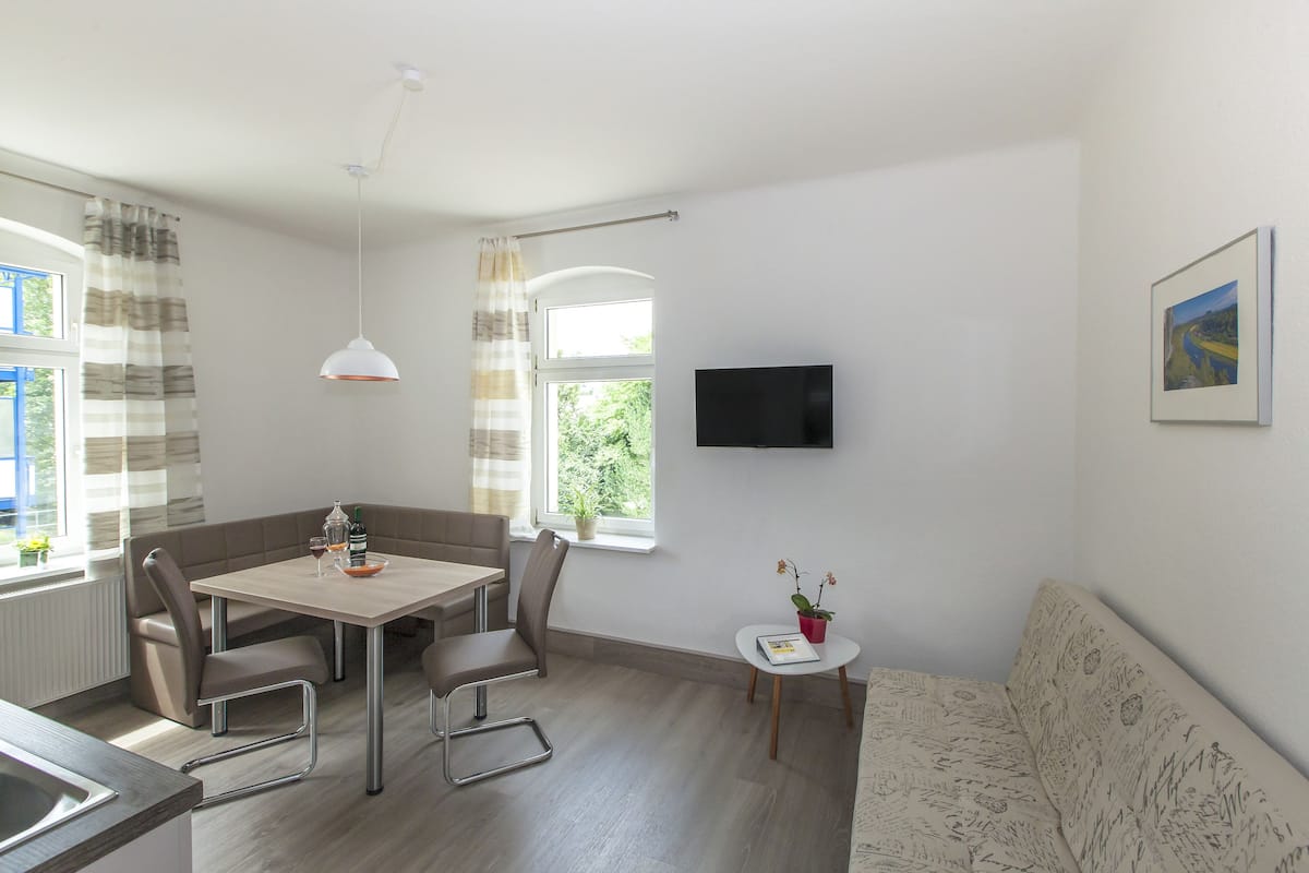 A modern room with a dining table, chairs, a sofa, a TV, and a window with curtains.