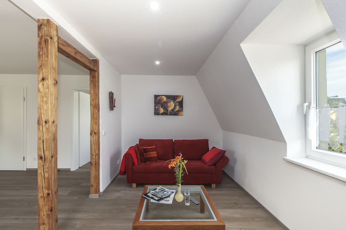 A modern living room with a red sofa, a glass coffee table with a vase, and a painting on the wall.