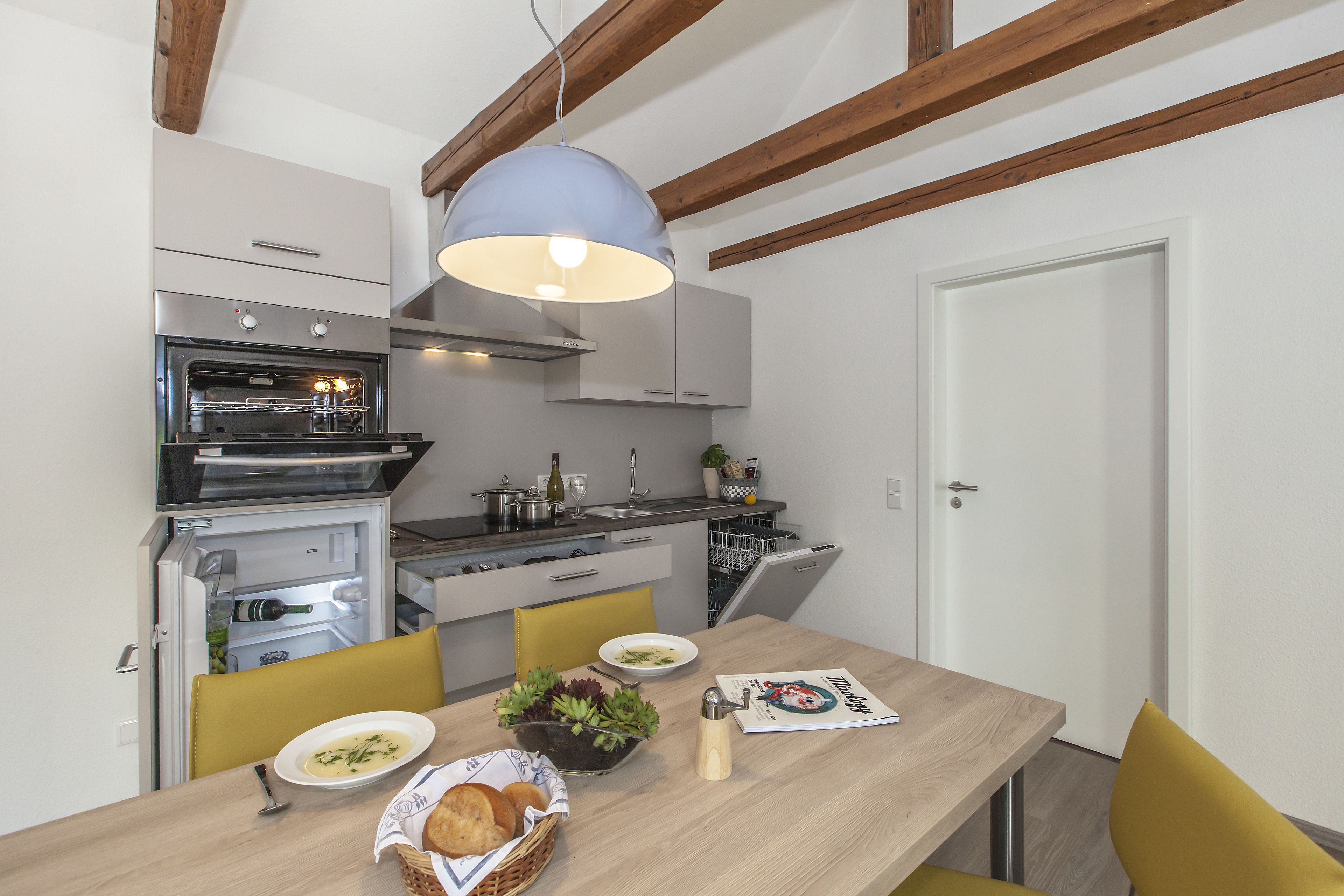 A compact kitchen with a built-in oven, a dining table with chairs, and a pendant light.