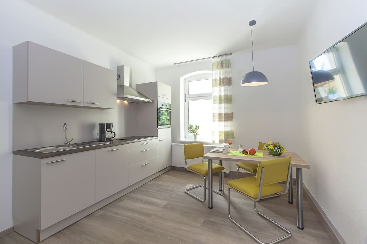 A modern kitchen with white cabinets, a built-in oven, and a dining area with yellow chairs and a table.
