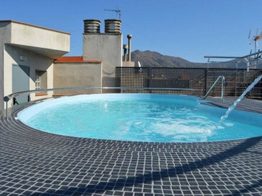 Une piscine sur le toit, avec une terrasse carrelée, une rambarde en métal et une vue imprenable sur les montagnes.